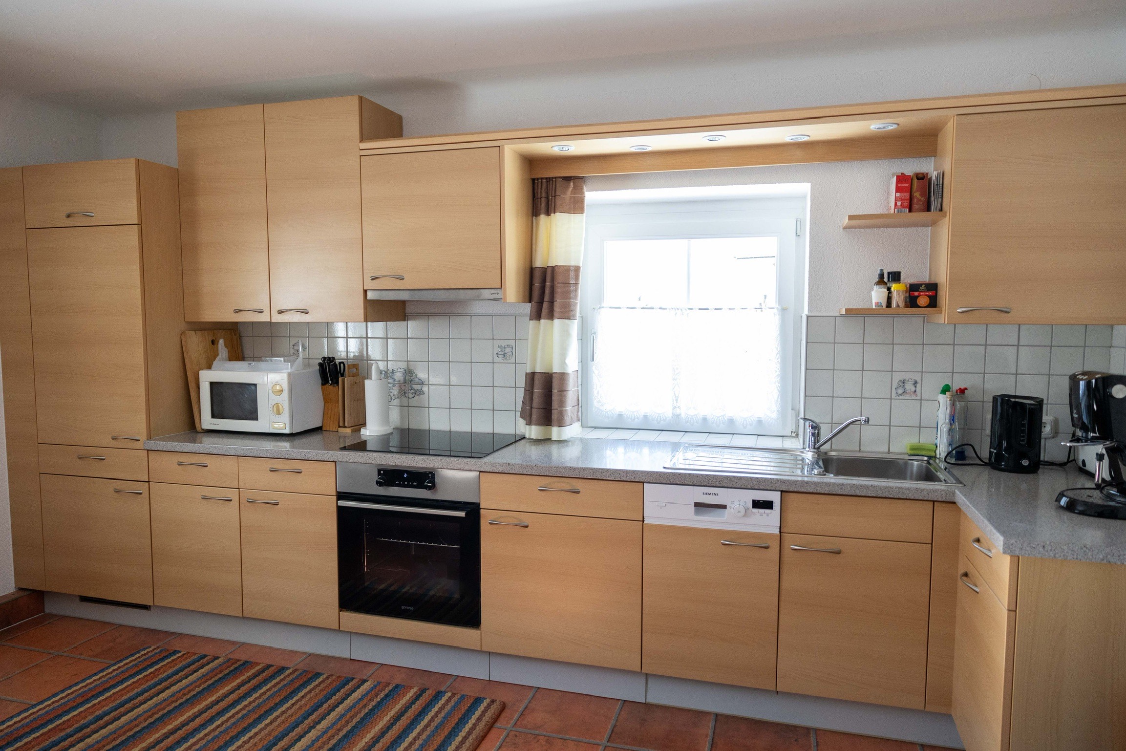 Die einladende Ferienwohnungs-Küche in Holzoptik mit Kühlschrank, Mikrowelle, Backofen, Elektroherd, Spülmaschine und Kaffeemaschine.